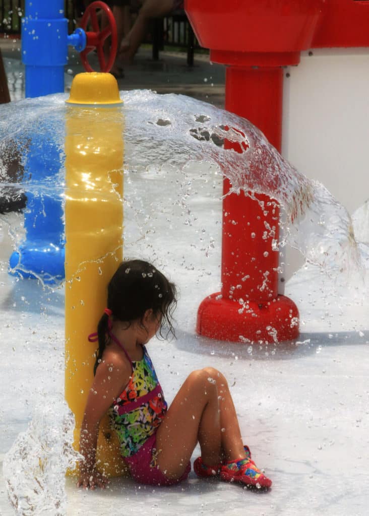 A female child sits underneath a water sprayer at the Splash Park